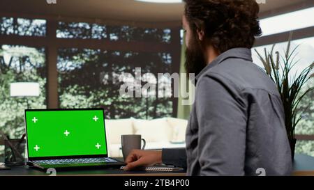 Der mächtige Tycoon entspannt sich in seinem beeindruckenden Herrenhaus in einem Wald und blickt auf den Grünbildschirm am PC. Global Enterprise Chairman verbindet sich mit einem Notebook mit leerem Copyspace, wohlhabendem Lifestyle. Stockfoto