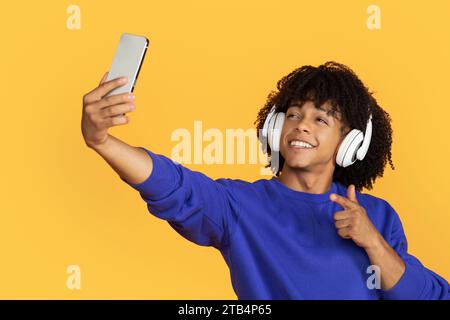 Glücklicher junger Schwarzer mit schnurlosen Kopfhörern, der Selfie mit dem Smartphone macht Stockfoto