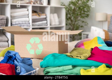 Ein Stapel Kleidung in verschiedenen Farben in einer Schachtel mit einem Recycling-Schild. Stockfoto