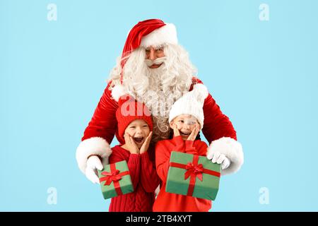 Überraschte kleine Kinder, die Weihnachtsgeschenke vom Weihnachtsmann auf blauem Hintergrund erhalten Stockfoto