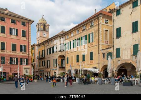 Piazza Vittorio Emanuele II, wo im Frühjahr Menschen in Cafés im Freien laufen und sitzen, Finale Ligure, Savona, Ligurien, Italien Stockfoto