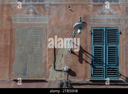Detail des Äußeren eines alten Hauses mit einem gefälschten Fenster, gemalt im Trompe l'oeil Stil, neben einem echten Fenster mit geschlossenen Fensterläden, Savona, Ligurien Stockfoto