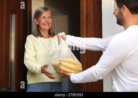 Nachbarn helfen. Mann mit Netztüte mit Produkten besucht Seniorinnen im Freien Stockfoto