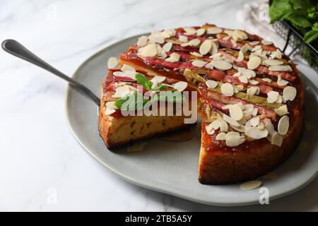 Frisch gebackener Rhabarberkuchen mit Mandelflocken und Tortenheber auf weißem Marmortisch, Nahaufnahme Stockfoto