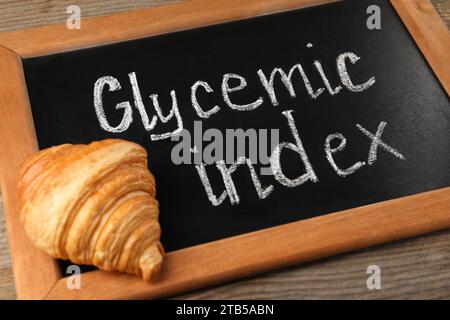 Kleine Tafel mit den Worten Glycemic Index und Croissant auf Holztisch, Nahaufnahme Stockfoto