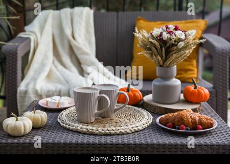 Rattan-Tisch mit Getränketassen, Croissants, Käse und Herbstdekor auf der Terrasse Stockfoto