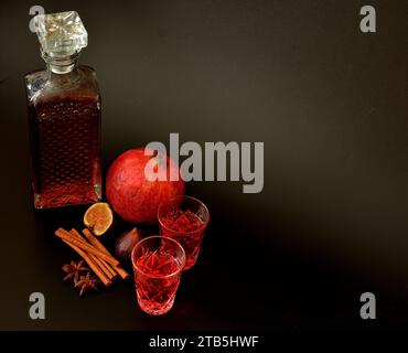 Feigen-Granatapfellikör mit Zimt und Anis auf schwarzem Hintergrund, starker hausgemachter Alkohol in einer Kristallkaraffe und zwei Gläsern, neben reifer fru Stockfoto