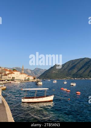 Perast, Montenegro - 03. august 2023: Kleine Boote liegen vor der Küste von Perast vor dem Hintergrund alter Häuser und der Kirche St. Nicholas Stockfoto