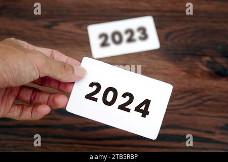 Die Hand nimmt die 2024-Karte und hinterlässt die 2023-Karte. Anfang des neuen Jahres 2024. Neujahrsvorbereitung, Leben, Geschäft, Pläne, Ziele, Ziele Stockfoto