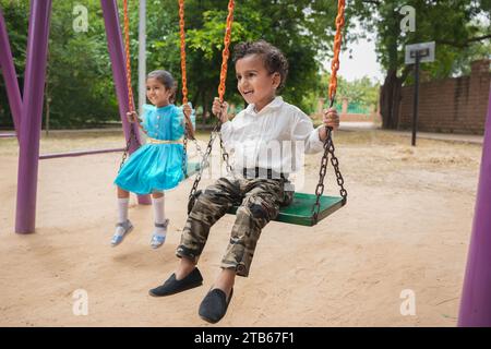 Zwei niedliche kleine indische Kinder, die sich gemeinsam auf einer Schaukel im wunderschönen Park oder Garten Vergnügen. Stockfoto