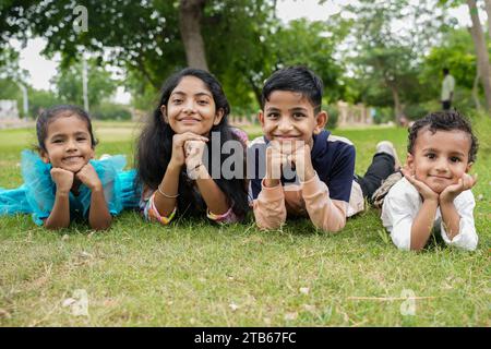 Eine Gruppe süßer indischer Kinder, die im Garten liegen und die Hände unter den Wangen in die Kamera schauen. Stockfoto