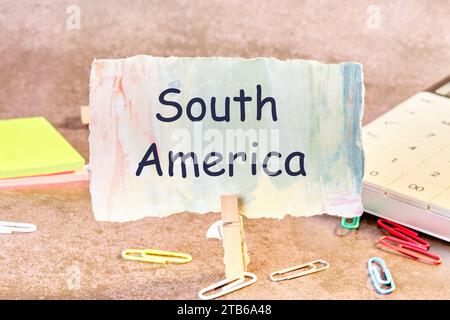 Südamerika-Phrase auf Papier geschrieben neben verstreuten Büroklammern, Taschenrechner, Klebepapier. Stockfoto