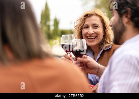 Freunde stoßen fröhlich Gläser Rotwein an und feiern gemeinsam einen freudigen Moment im Freien. Stockfoto