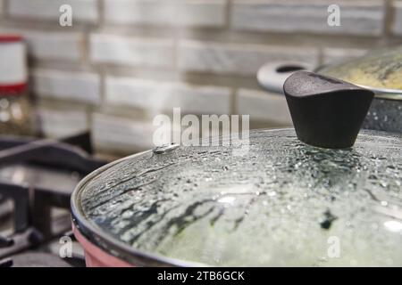 Nahaufnahme eines Deckels einer Glaspfanne mit steigendem Dampf und Wassertropfen, die auf der Oberfläche kondensieren, was darauf hinweist, dass die Pfanne für Co-Zwecke verwendet wird Stockfoto