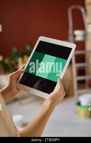 Vertikales Bild einer jungen Frau, die ein digitales Tablet hält und Farbe für die Gestaltung der Wohnung wählt Stockfoto