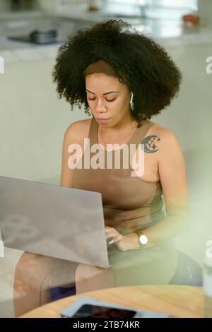 Ernsthafte Frau, die auf Fitnessball sitzt und am Laptop arbeitet Stockfoto