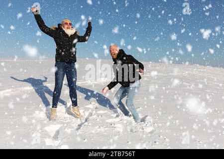 Ein junges Paar, bestehend aus einer Frau und einem Mann, springt in die Luft im Schnee und hat Spaß miteinander Stockfoto
