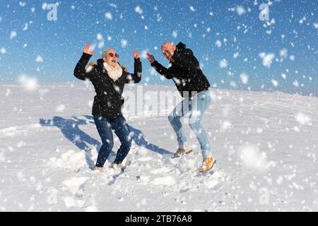 Ein junges Paar, bestehend aus einer Frau und einem Mann, springt in die Luft im Schnee und hat Spaß miteinander Stockfoto