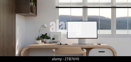 Vorderansicht eines PC-Computers mit weißem Bildschirm auf einem modernen Holzschreibtisch vor dem Fenster in einem modernen Zimmer. Heim-Arbeitsplatz, privates Büro Innenraum i Stockfoto