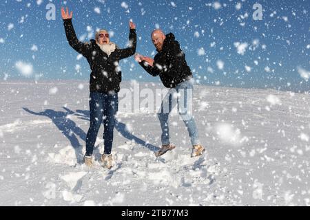 Ein junges Paar, bestehend aus einer Frau und einem Mann, springt in die Luft im Schnee und hat Spaß miteinander Stockfoto