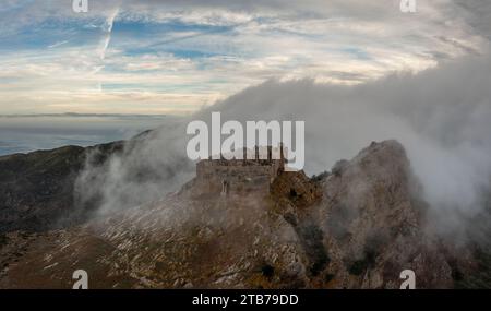 Magazzini, Italien - 14. November 2023: Drohnenblick auf das Castello del Volterraio, umgeben von Morgennebel und Wolken Stockfoto