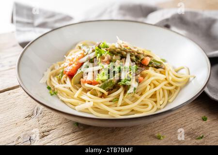 Spaghetti mit Gemüsesauce aus grünem Spargel und Tomaten mit Parmesan und Petersilie garnieren auf einem Teller auf einem rustikalen Holztisch, ausgewählter Fokus, Stockfoto