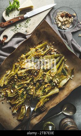 Köstlicher gebratener Fenchel mit Nüssen auf Backblech auf dem Küchentisch mit Utensilien, Blick von oben Stockfoto