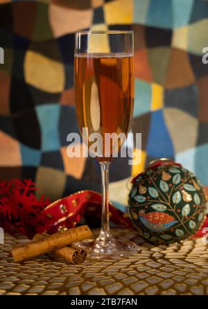 Hohes Glas Champagner mit Weihnachtsdekoration, darunter zwei Zimtstangen, eine grüne Kugel, eine rote Schneeflocke vor einem Gemälde Stockfoto