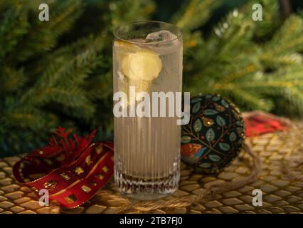 Gin Tonic in Hochkugelglas mit Zitrone und Eis mit Glaskugeldekorationen vor einem Kiefernzweig Stockfoto