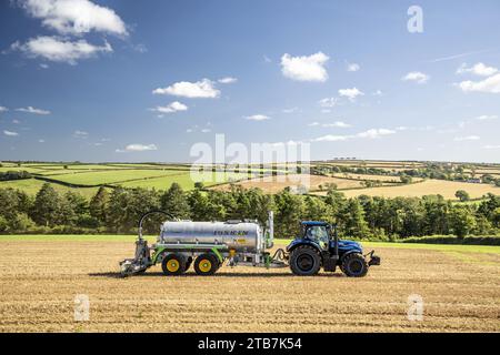 Grossbritannien: Cornwalls landwirtschaftliche Landschaft. New Holland T7 LNG-Traktor (Liquefied Natural Gas) mit Joskin Advantage Schlammtanker auf dem Feld Stockfoto