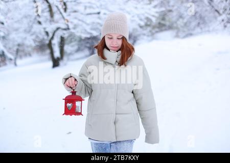 Mädchen in Winterkleidung Kapuze geht mit einer brennenden Laterne durch den verschneiten Wald. Stockfoto
