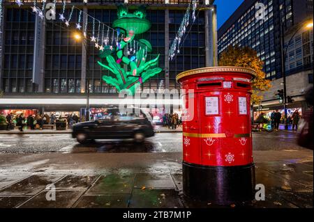 London, Großbritannien. Dezember 2023. Ein königlicher Briefkasten (gegenüber John Lewis) ist als weihnachtsgeschenk bemalt und spielt Weihnachtslieder, wenn ein Brief verschickt wird - trotz des kalten und nassen Wetters gibt es in der Oxford Street viele Leute, die früh einkaufen gehen, wenn die Weihnachtszeit anhält. Guy Bell/Alamy Live News Stockfoto