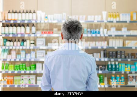 Rückansicht eines anonymen älteren Mannes mit grauem Haar, der aus verschiedenen Produkten in Regalen im Pharmageschäft steht Stockfoto