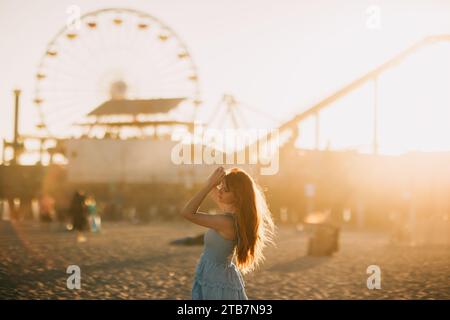 Eine ruhige Szene fängt eine Frau am Santa Monica Pier mit einem unscharfen, legendären Riesenrad im Hintergrund ein. Der goldene Sonnenuntergang taucht alles in einen Krieg Stockfoto