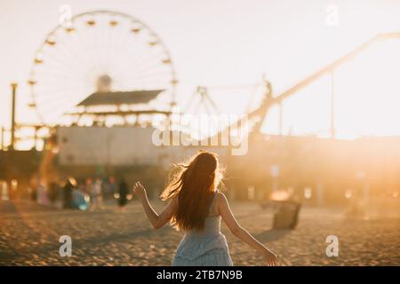 Frau, die einen traumhaften Sonnenuntergang am Riesenrad am Santa Monica Pier genießt, verkörpert die Essenz des legendären Vergnügens am Meer von Los Angeles. Stockfoto