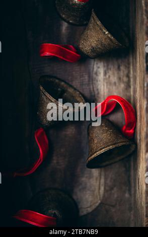Ästhetische Nahaufnahme rustikaler Metallglocken mit leuchtenden roten Bändern, präsentiert auf einer strukturierten Holzoberfläche, die ein Gefühl von Tradition weckt. Stockfoto