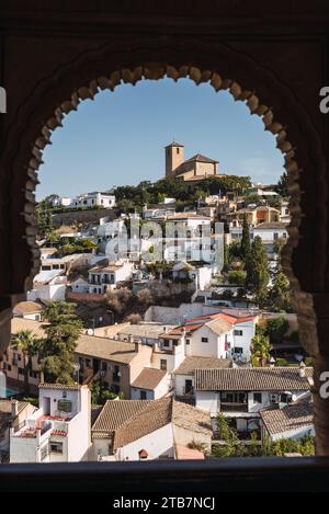 Wunderschöner Blick auf das Stadtbild mit Glockenturm und Wohngebäuden auf einem Hügel vor klarem Himmel, durch das Bogenfenster des Generalife Palastes in Grana Stockfoto