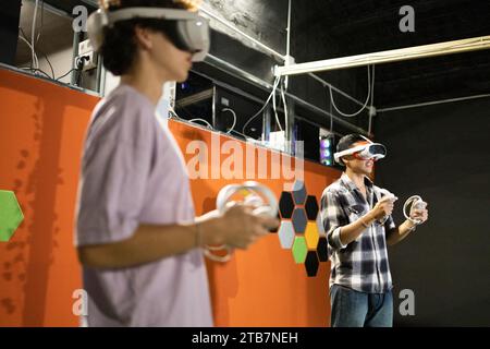 Zwei Personen, die an einer immersiven Virtual-Reality-Gaming-Session teilnahmen, verwendeten VR-Headsets und Handheld-Controller. Stockfoto