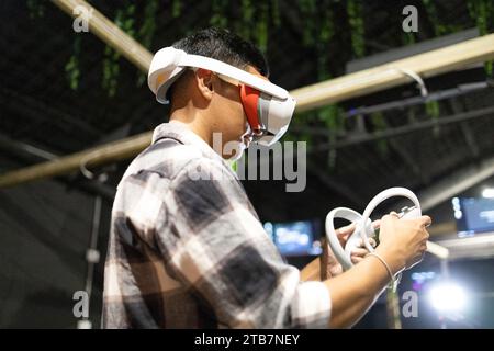 Ein junger Mann, der in eine virtuelle Realität eingetaucht ist und Handheld-Controller bei einem Gaming-Event verwendet. Stockfoto