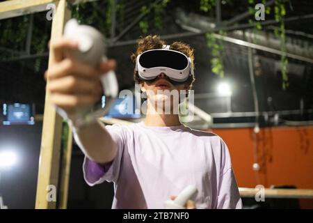 Von unten ist ein junger aufgeregter Mann in einem Virtual-Reality-Spiel mit einem VR-Headset und mit Controllern verwickelt Stockfoto