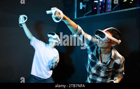 Zwei Personen spielen gerne ein interaktives Spiel, während sie Virtual-Reality-Headsets verwenden und Bewegungen mit Controllern anzeigen. Stockfoto