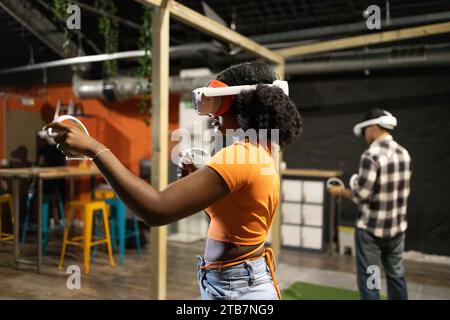 Seitenansicht junger multirassischer Freunde, die in Virtual-Reality-Spielen mit VR-Headsets und Handheld-Controllern in Innenräumen spielen Stockfoto