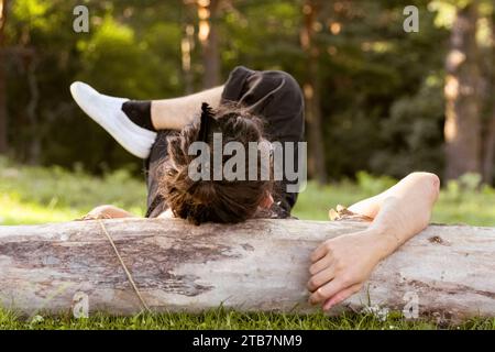 Eine entspannte anonyme Person, die auf einem gefallenen Baumstamm in einem üppigen Wald liegt, umgeben von grünem Gras, und einen ruhigen Moment genießt Stockfoto