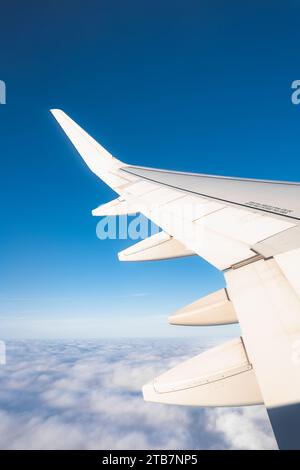 Ernteflügel eines Flugzeugs, das bei sonnigem Wetter über weiße Wolken gegen blauen Himmel fliegt Stockfoto