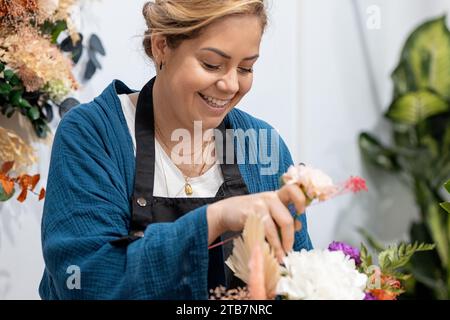 Blumenlächeln, während sie einen schönen Blumenstrauß in ihrem Geschäft mit einem stilvollen Hintergrund aus Blumen arrangieren Stockfoto