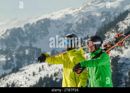 Zwei Skifahrer in leuchtenden Jacken tragen ihre Skier auf der Schulter und sind bereit, die schneebedeckten Pisten der Schweizer Alpen zu bewältigen und einen Wintersportler zu präsentieren Stockfoto