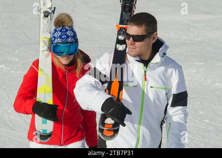 Ein fröhliches Paar, das Ski auf einem schneebedeckten Berghang trägt, sich im Sonnenschein sonnt und die Schönheit der Schweizer Alpen genießt Stockfoto