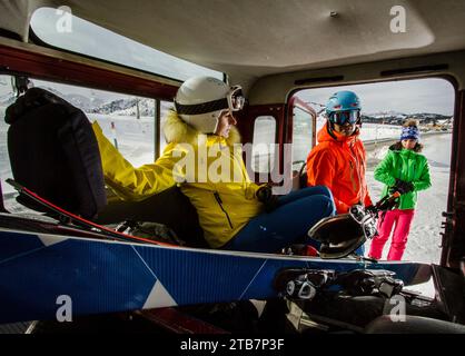 Eine Gruppe von Skifahrern in farbenfroher Ausrüstung macht sich in einem Fahrzeug vor einer verschneiten Bergkulisse bereit. Stockfoto