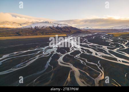 Ein atemberaubender Luftbild aus gewundenen, geflochtenen Flussmustern inmitten des schwarzen vulkanischen Sandes und der grünen Landschaft an den Ausläufern des schneebedeckten Berges Stockfoto