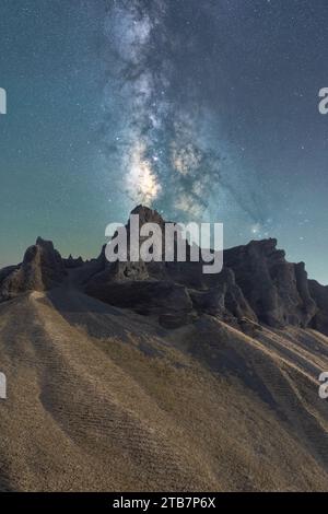 Die Magnificent Milky Way erhebt sich über einem zerklüfteten felsigen Gelände und der intensive Kern der Galaxie strahlt in näherer Nähe ein himmlisches Leuchten auf die irdische Landschaft aus Stockfoto